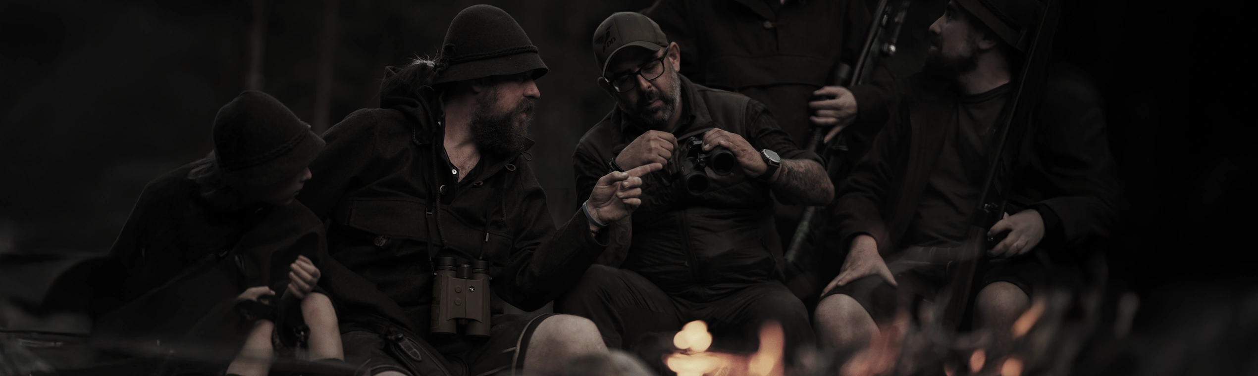 Hunters around a campfire, with brown DDoptics UltraView Range binoculars hanging in front of one hunter’s torso